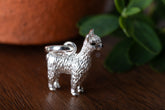 Silver llama-shaped charm on a wooden surface with a blurred plant in the background